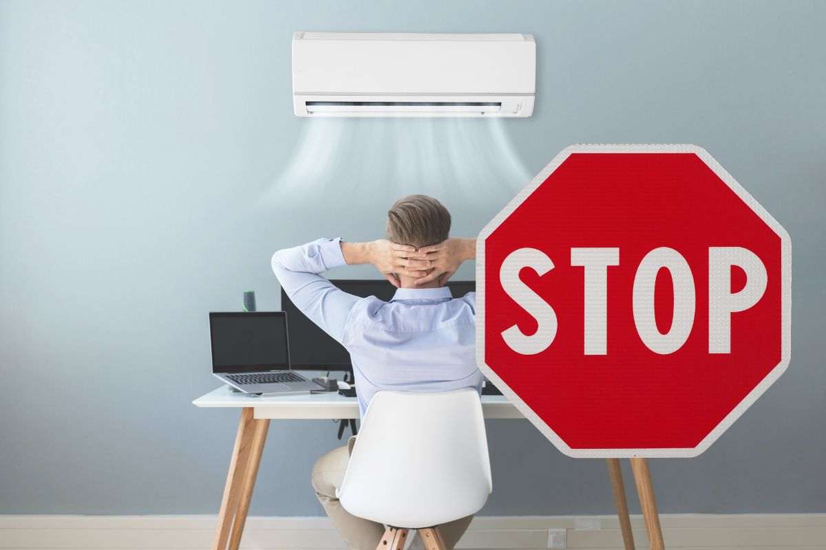 uomo davanti l'aria condizionata e cartello dello stop